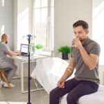 IV hydration vs drinking water comparison showing a man drinking water while receiving IV fluids in a medical clinic.
